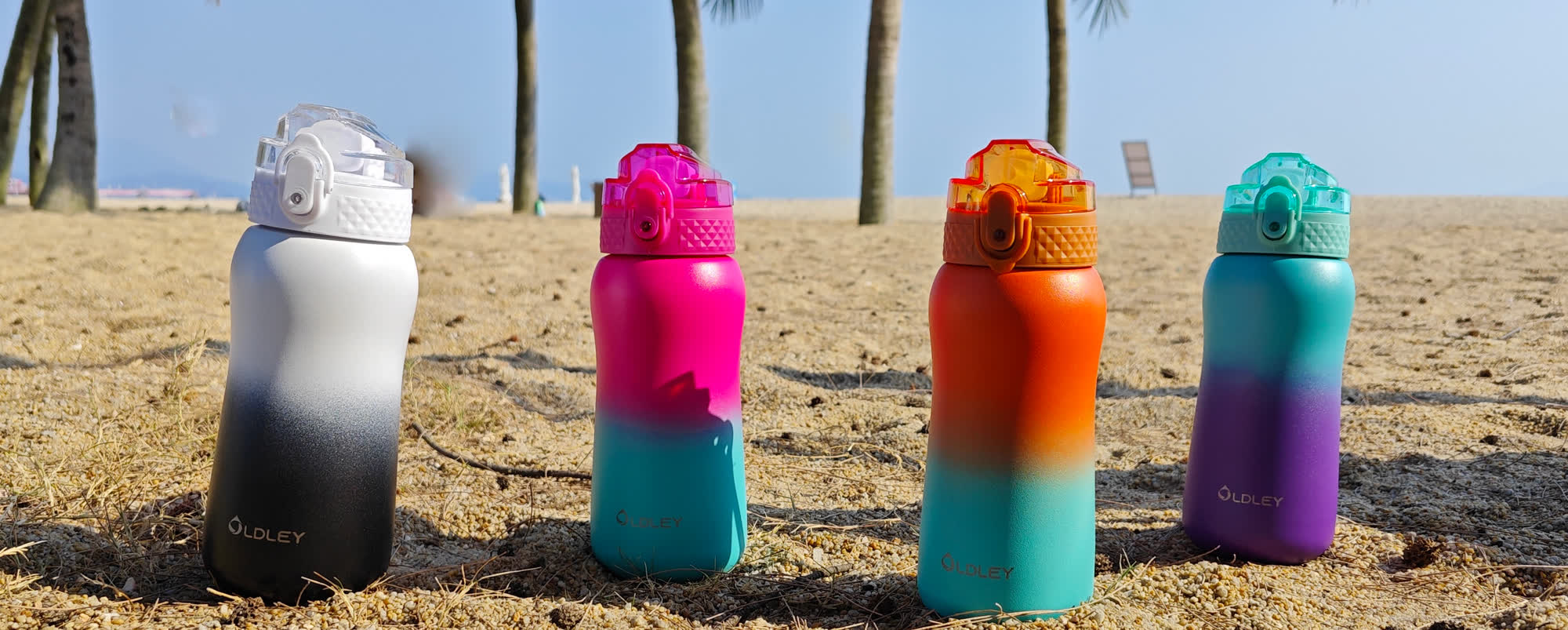 four gradient colored water bottles standing on sandy ground with palm trees