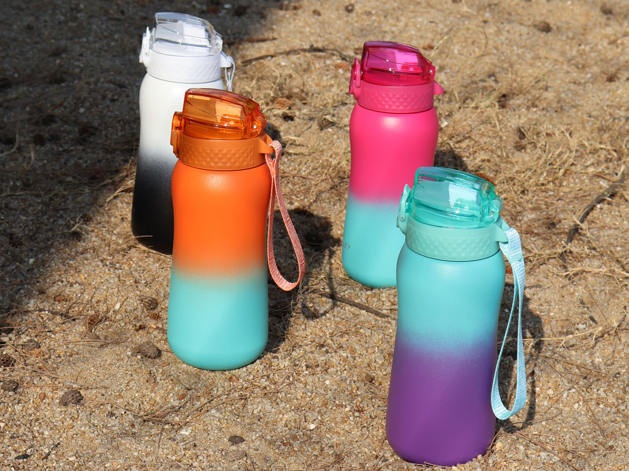 four gradient water bottles in white black orange pink and teal standing on sand