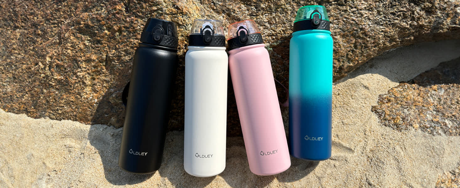 four solid color water bottles in black white pink and teal blue gradient standing on sand