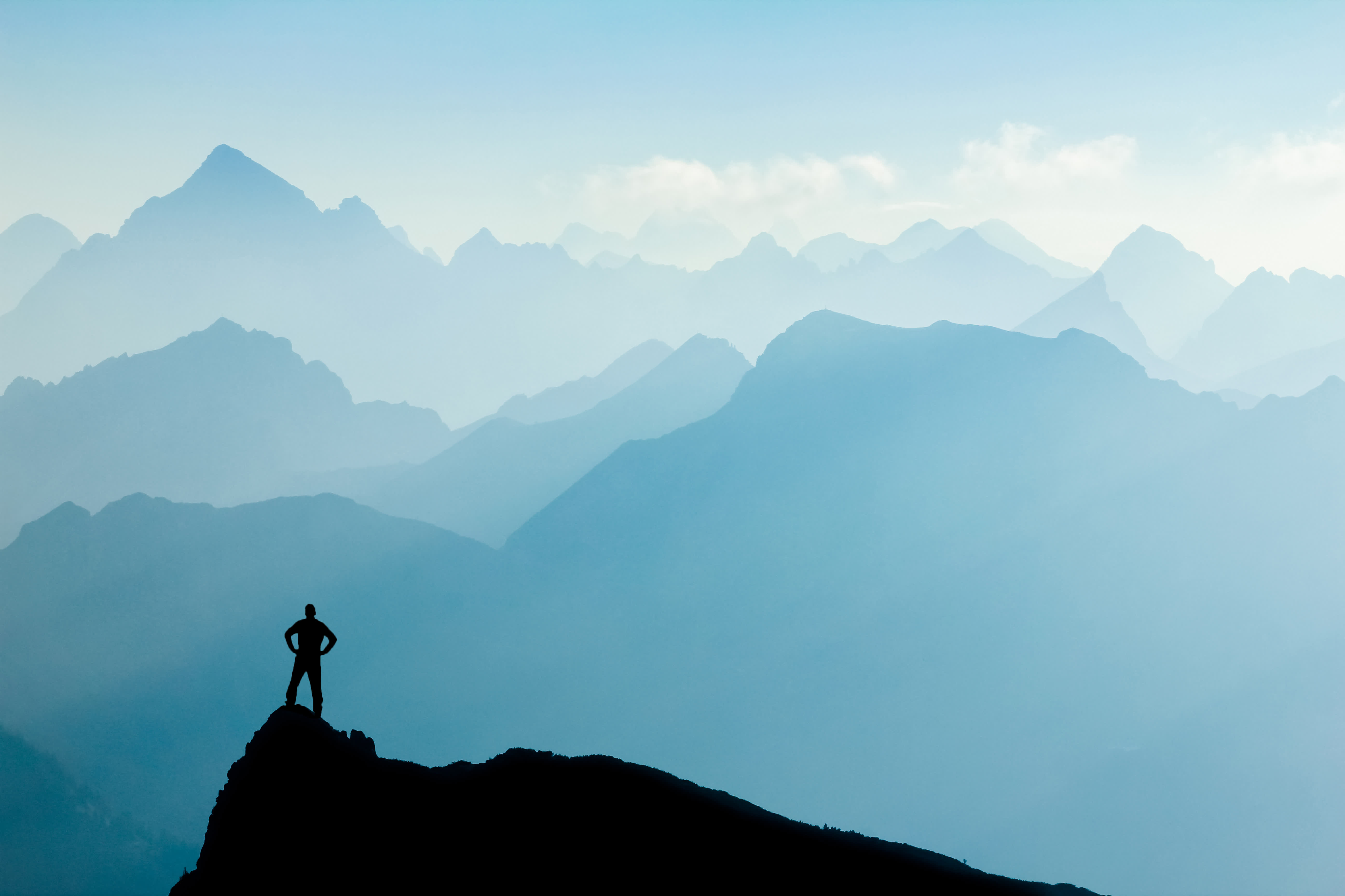 silhouette of person standing on mountain peak with layered blue misty mountains in background