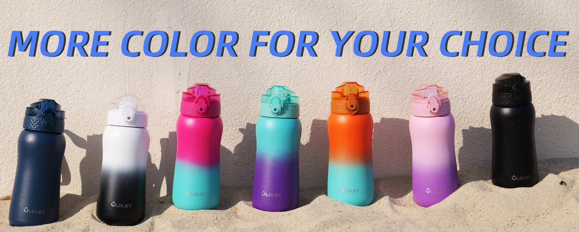seven gradient colored water bottles in row displayed on sand in front of concrete wall
