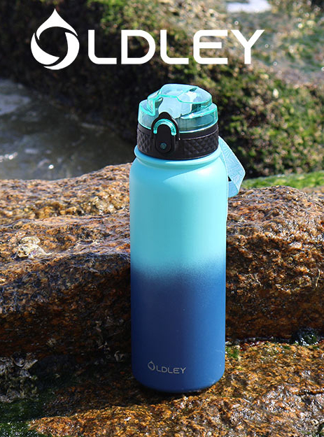 blue to navy gradient water bottle standing on mossy rocks near ocean water with brand logo