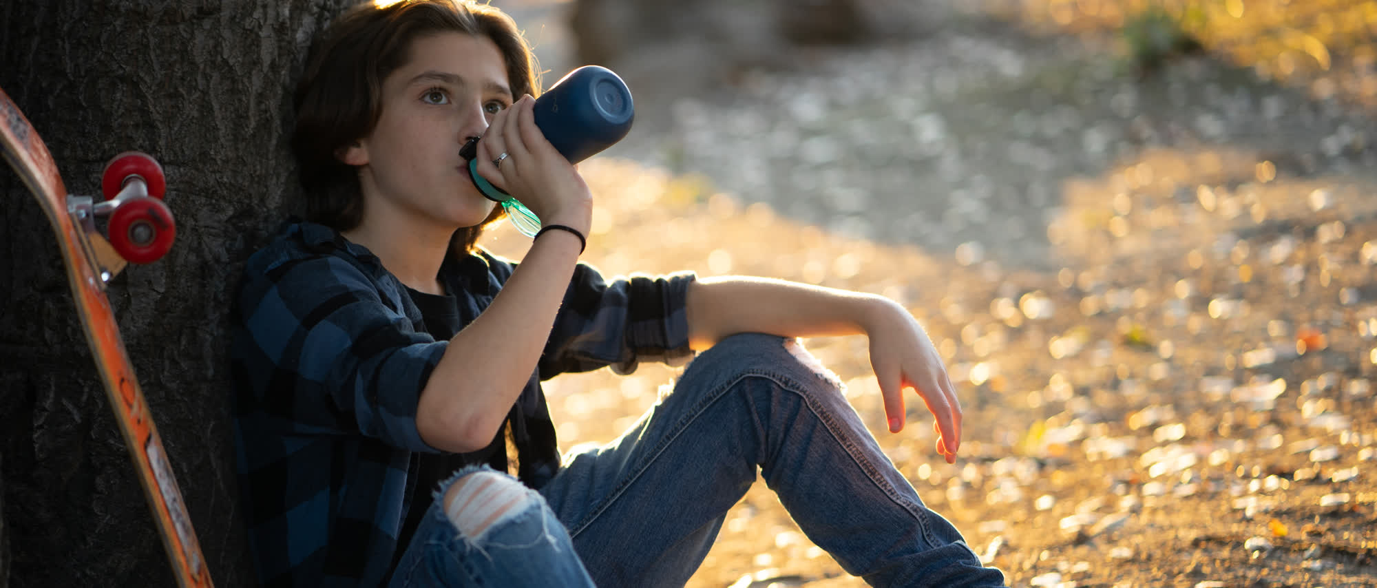 girl in blue plaid shirt drinking from blue water bottle under tree