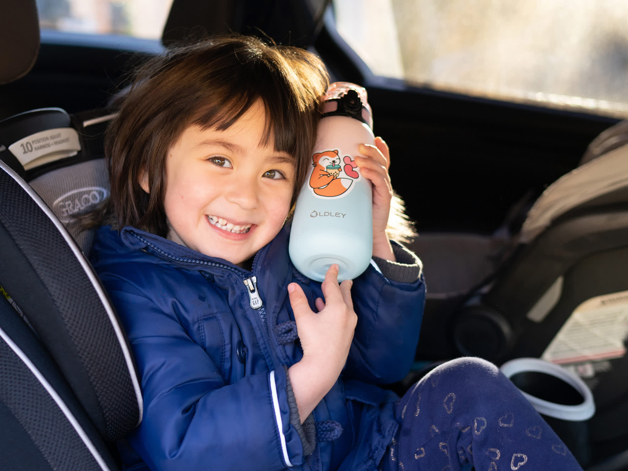 smiling child in blue jacket holding light blue water bottle with animal design