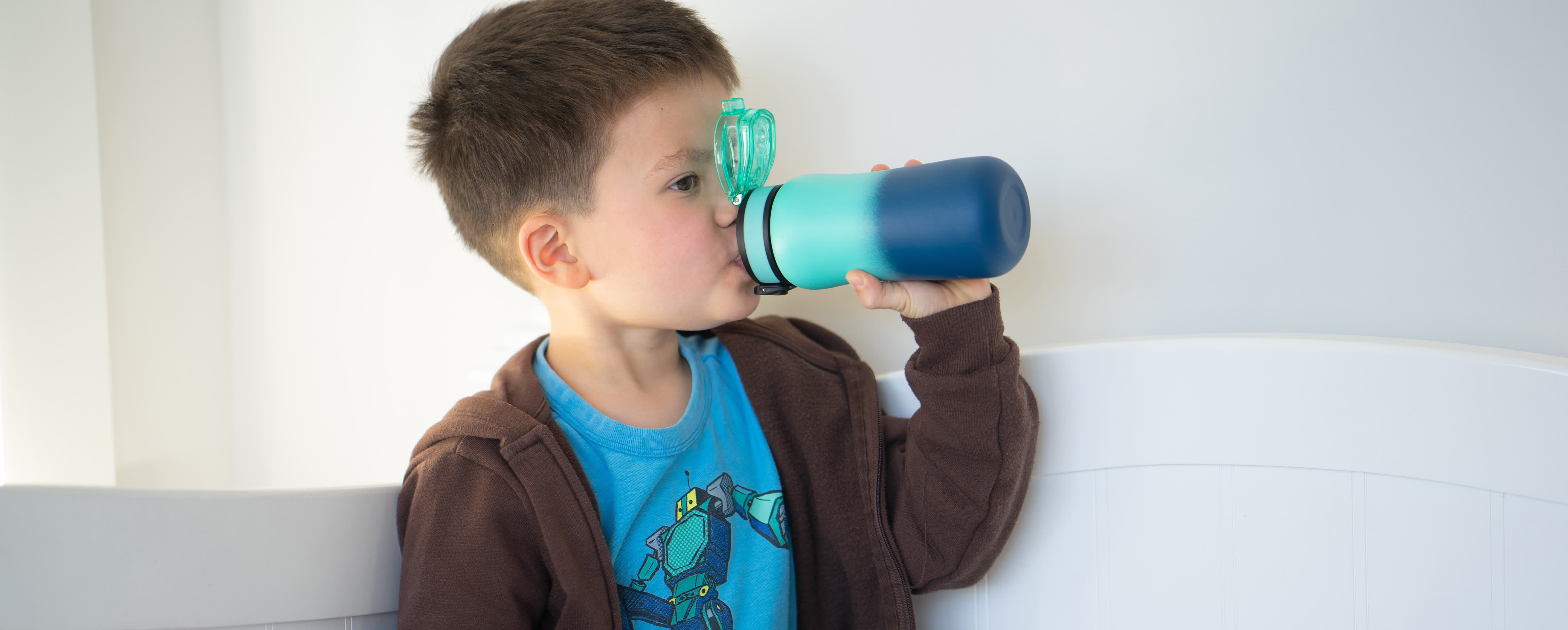 young boy in brown hoodie drinking from blue ombre water bottle
