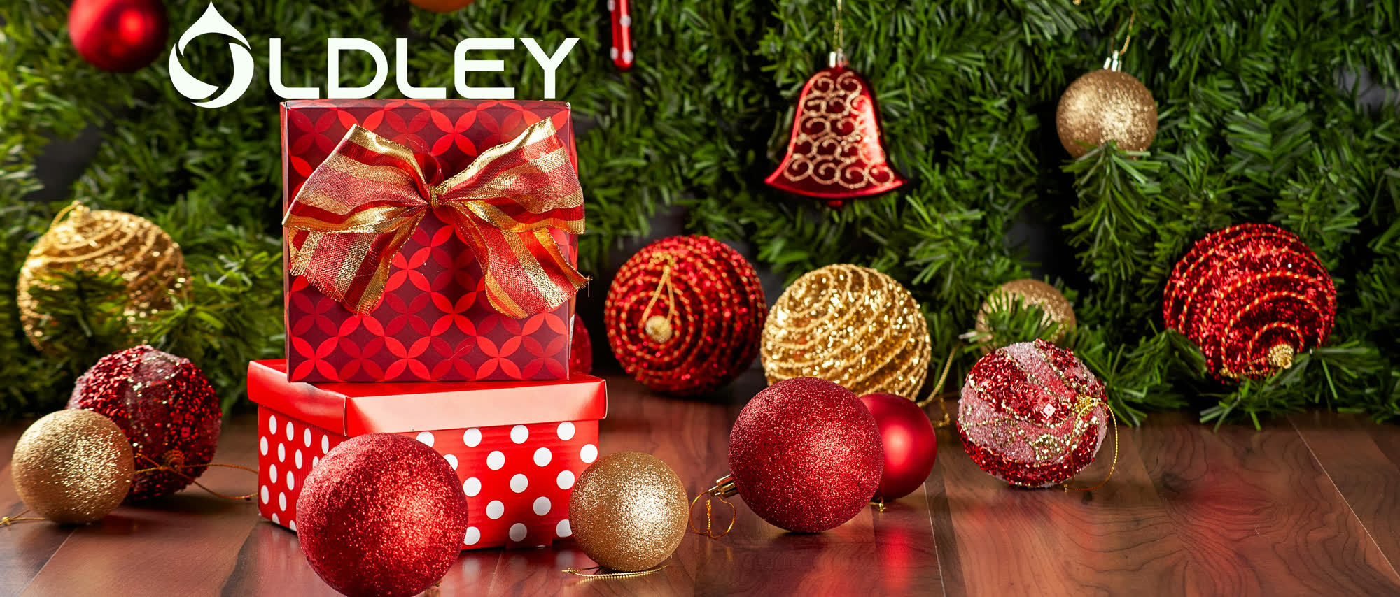 red gift boxes with gold bow surrounded by red and gold christmas ornaments with green garland
