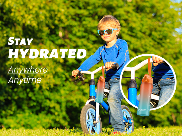 young boy in blue sunglasses and blue long sleeve shirt riding blue bicycle on green grass with gradient water bottle