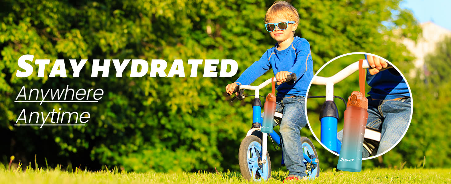 young boy in blue sunglasses and blue shirt riding bicycle on green grass with gradient water bottle attached to handlebars